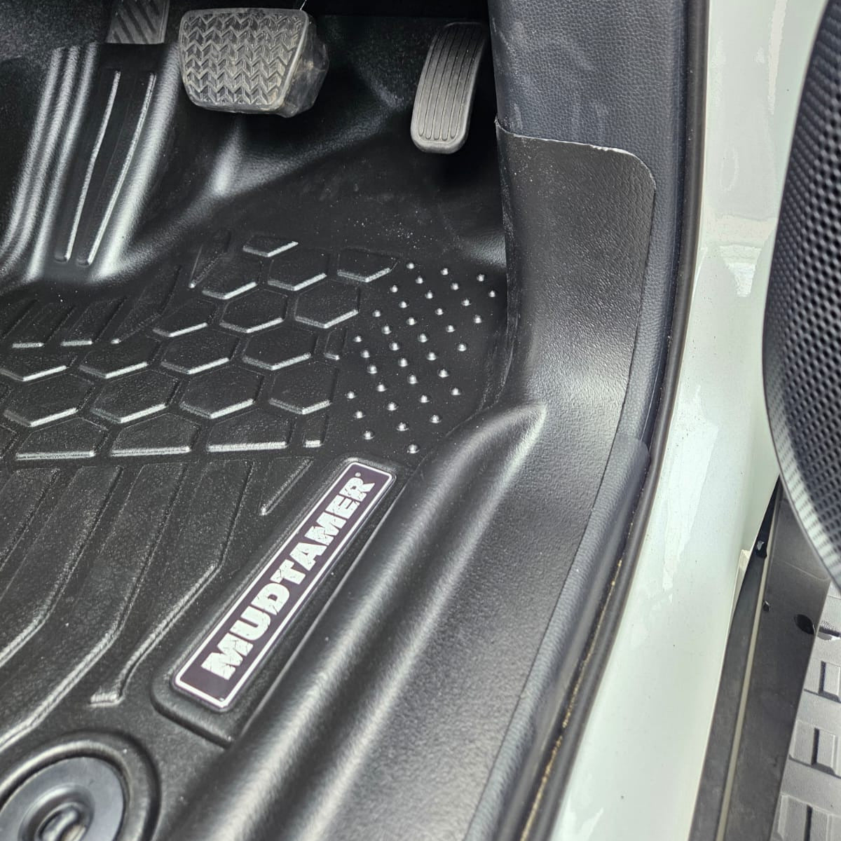 Car floor mat with 'MudTamer' branding inside a vehicle.